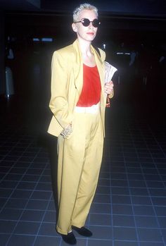 a woman in a yellow suit and red top standing on tiled floor with her hands in her pockets