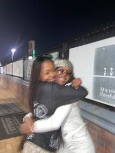 two women hugging each other in front of a street sign at night with the lights on