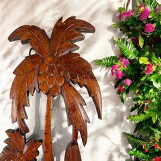 a wooden palm tree hanging from the side of a wall next to pink flowers and greenery