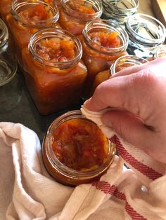 a person holding a jar with some food in it on top of a table next to other jars