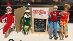 three elf dolls sitting next to a chalk board