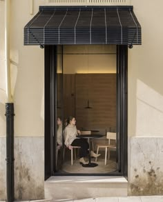 two people sitting at a table in front of a building with a black awning