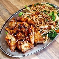 a plate filled with chicken, noodles and broccoli on top of a wooden table