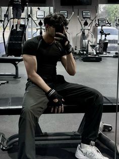 a man sitting on top of a bench in a gym holding a cell phone to his ear