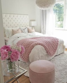 a white bedroom with pink flowers in the vase on the bed and a large window