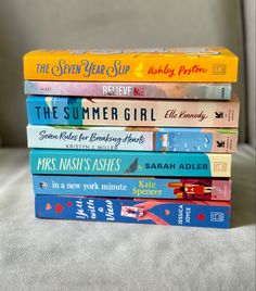 a stack of children's books sitting on top of a bed in front of a window