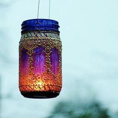 a purple and blue mason jar hanging from a hook on a window sill with a sky in the background