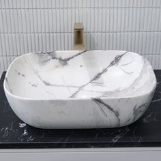 a white marble bowl sink sitting on top of a black counter next to a faucet