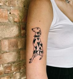 a black and white dog tattoo on the left upper half of the arm, next to a brick wall