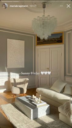 a living room filled with white furniture and a chandelier hanging from the ceiling