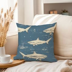 a pillow with sharks on it sitting on a couch next to a cup and saucer