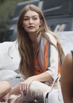 a woman with long hair sitting on the ground next to a white bag and purse