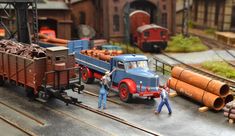 two men are working on a model train track with other toy trains in the background