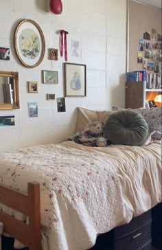 a bed with a teddy bear sitting on top of it next to a wall full of pictures