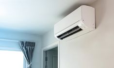 an air conditioner mounted to the side of a wall next to a window with curtains