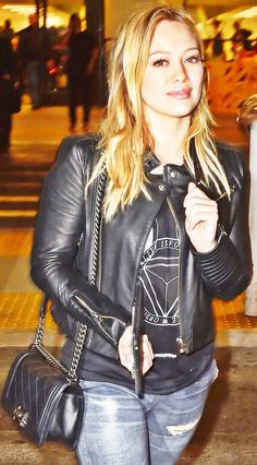 a woman is walking down the street with her hand in her pocket and wearing a black leather jacket