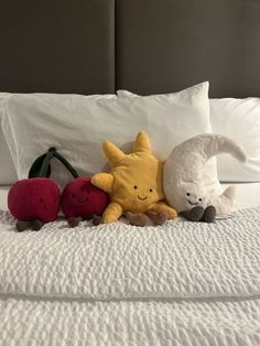 three stuffed animals are laying on a bed with white sheets and pillows, one is yellow