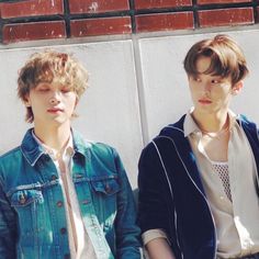 two young men sitting next to each other in front of a white wall with red bricks