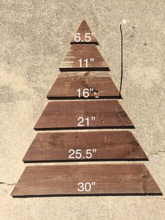 a wooden christmas tree sitting on top of a cement floor next to a measuring ruler