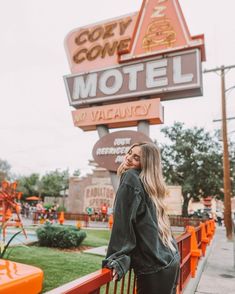 a woman standing in front of the neon motel sign with her hands on her hips