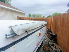 an rv parked next to a wooden fence in the back yard with a mattress on top