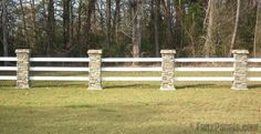 three stone pillars in front of a white fence with trees in the backround