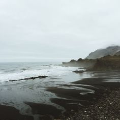 the beach is covered in black sand and water with waves coming up to it's shore