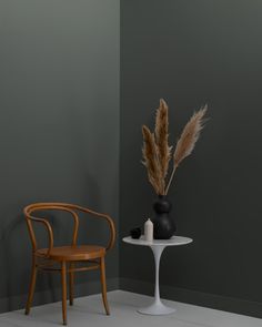 a chair next to a table with a vase on it and a plant in the corner