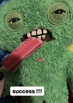 a green stuffed animal with an ice cream stick sticking out of it's mouth