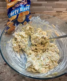 a glass bowl filled with food next to a bag of chips