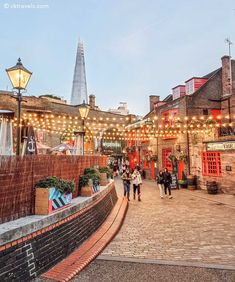 people are walking around in an outdoor area with lights strung up on the buildings and street lamps