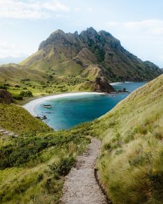 a path leading to a beach on the side of a mountain with blue water and mountains in the background