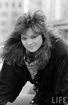 a black and white photo of a woman leaning on a car trunk with her hair blowing in the wind