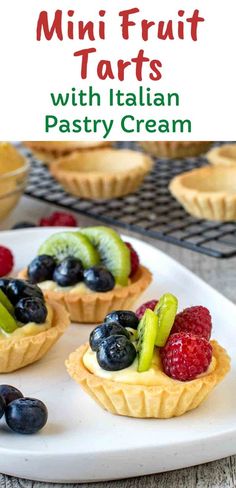 mini fruit tarts with italian pastry cream on a white platter next to berries and kiwis