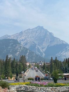 the mountains are covered with snow in the background and people walking on the sidewalk below