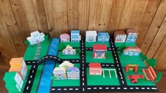 a paper model of a city with roads and buildings on it's sides is shown in front of a wood paneled wall