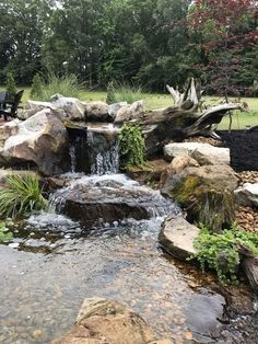 there is a small waterfall in the middle of some rocks and grass near a bench