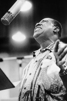 a black and white photo of a man singing into a microphone with his hands in the air