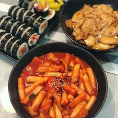 three black bowls filled with food on top of a white tableclothed countertop