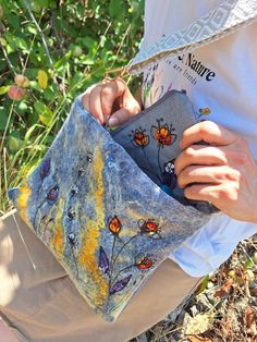 a woman is holding a purse with butterflies on it in front of some grass and bushes