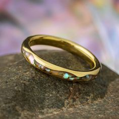 a gold wedding band with opalite stones on top of a rock in front of a colorful background