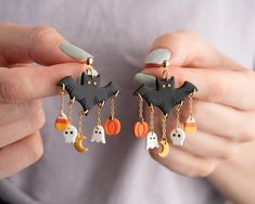 a woman holding two halloween themed earrings in her hands