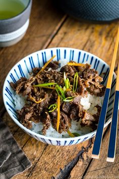 a close up of a bowl of food with chopsticks on the table next to it