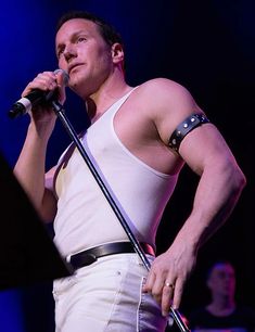 a man standing in front of a microphone on stage with his hands behind his back