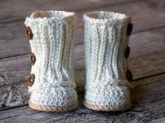 a pair of white knitted boots with buttons on the inside and outside, sitting on a wooden surface