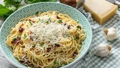 a bowl of pasta with parmesan cheese and herbs on the table next to garlic