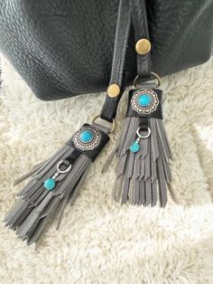 two tassels with turquoise beads are hanging from a black leather bag on a white carpet