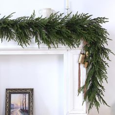 a white fireplace mantel decorated with greenery and bells