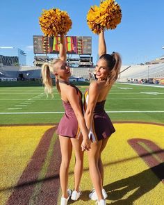 two cheerleaders holding up pom - poms in front of the football field