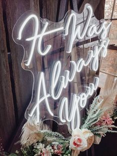 a neon sign that says it always happens with flowers in front of an old wooden wall